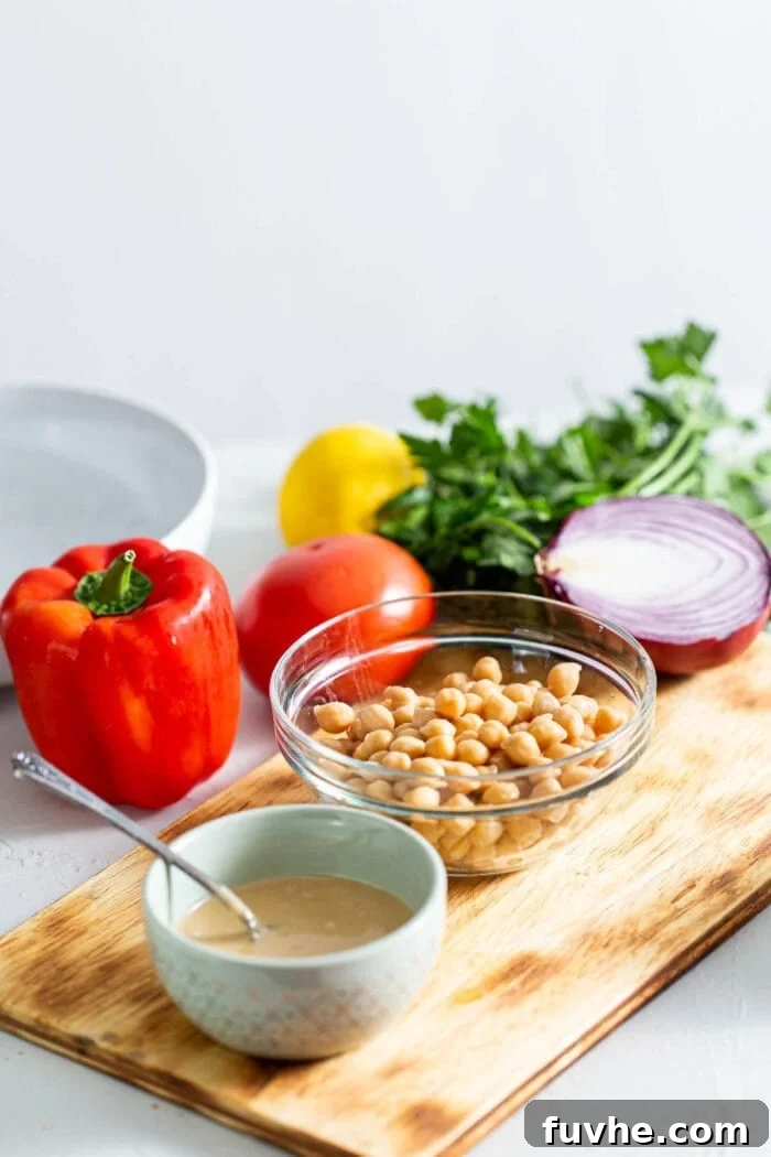 Chickpeas, tahini, bell pepper, onion, parsley and red onion on a cutting board.