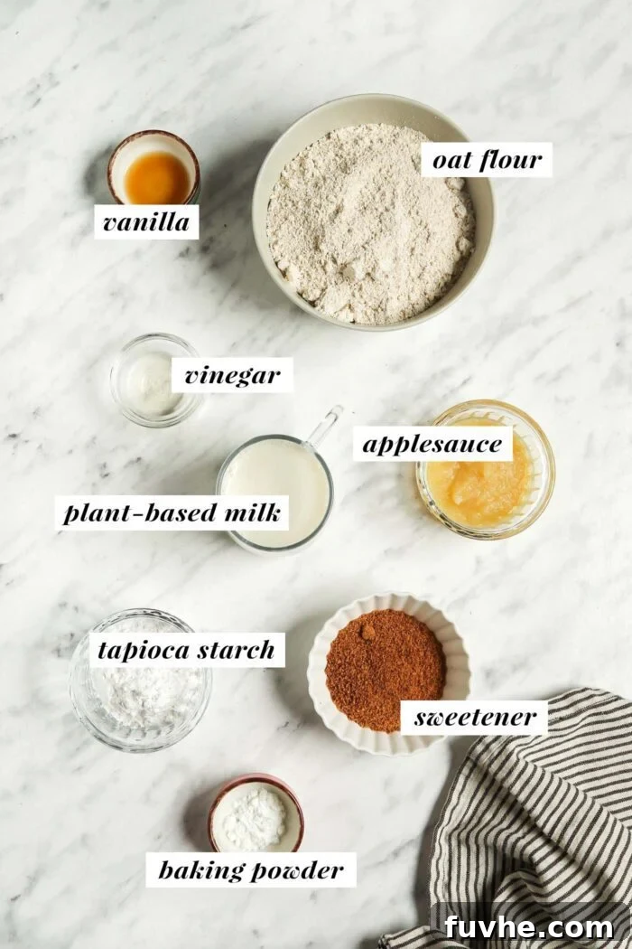 Oat flour, tapioca starch, sugar, vanilla and baking powder in small bowls on a marble surface. Each ingredient is labelled with text.