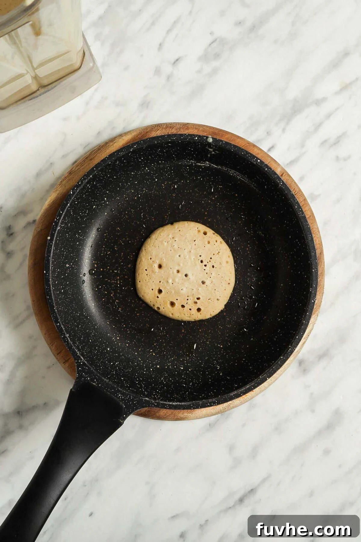 A vegan and gluten-free oat banana pancake cooking in a small nonstick pan.