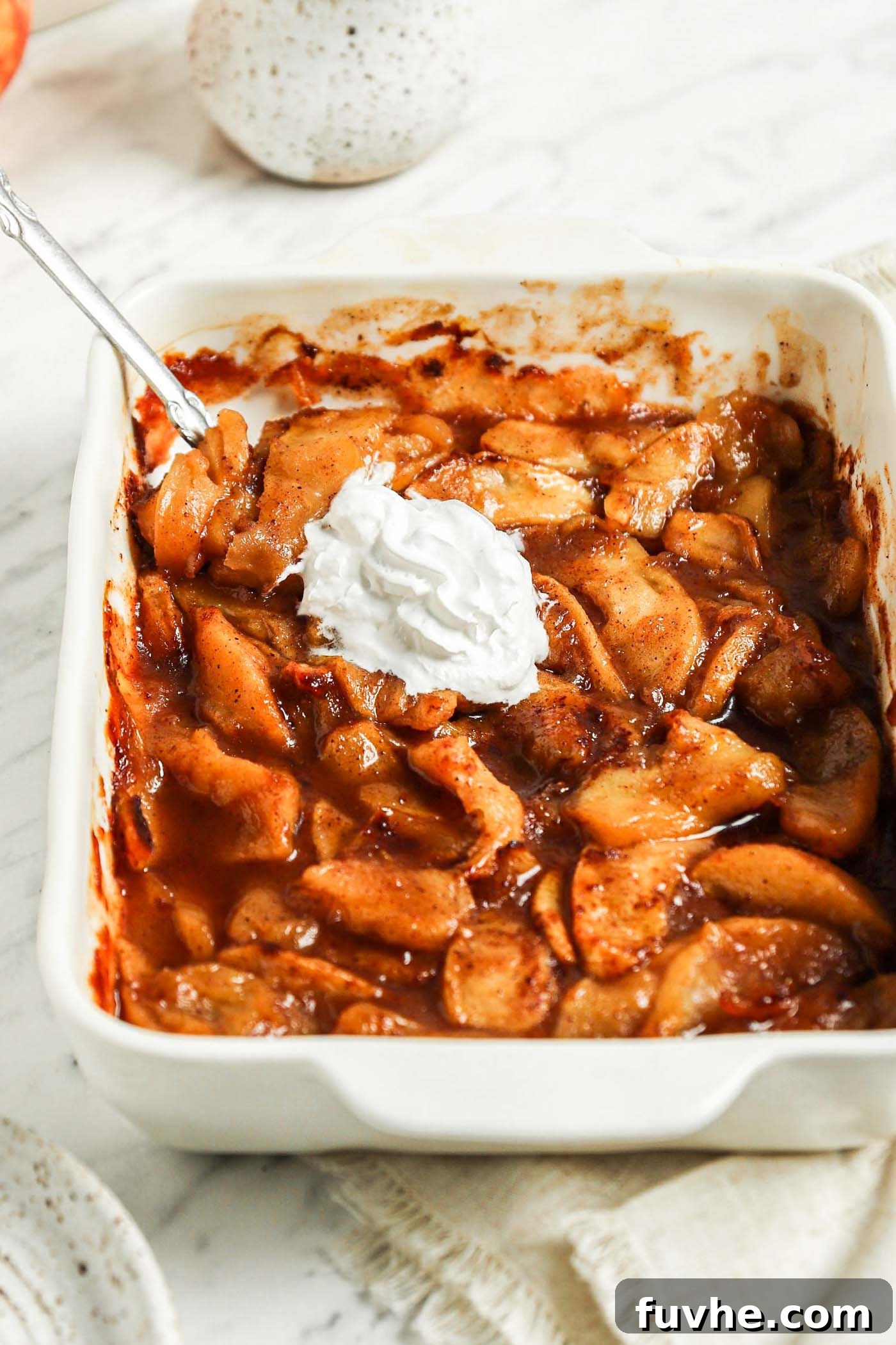 Casserole dish of sliced baked apples topped with whipped cream.