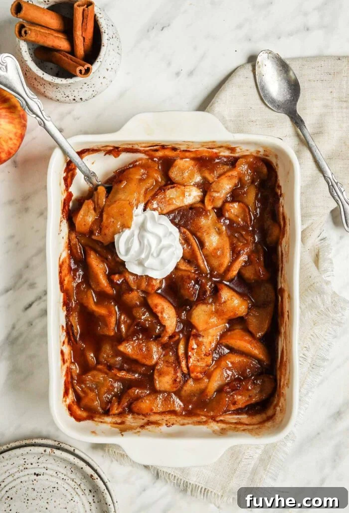 Casserole dish of sliced baked apples topped with whipped cream.