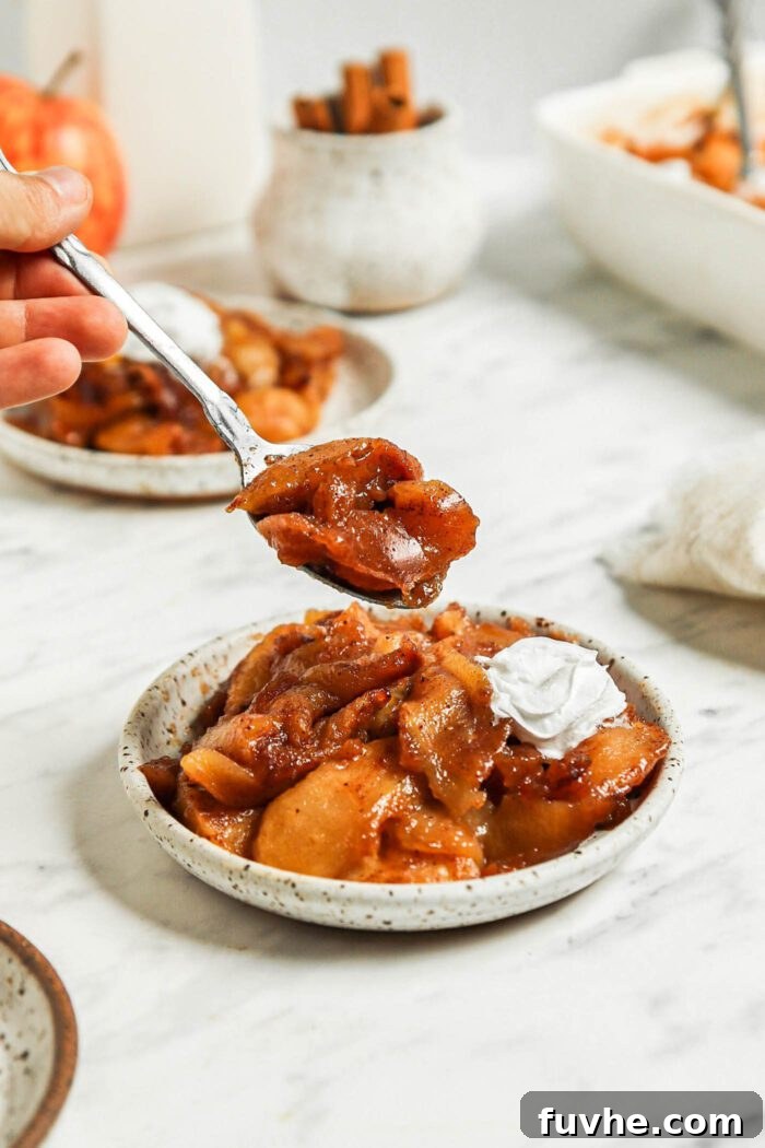 Small spoon taking a spoonful of cinnamon baked apples from a plate.
