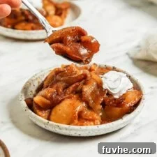 Small spoon taking a spoonful of cinnamon baked apples from a plate.