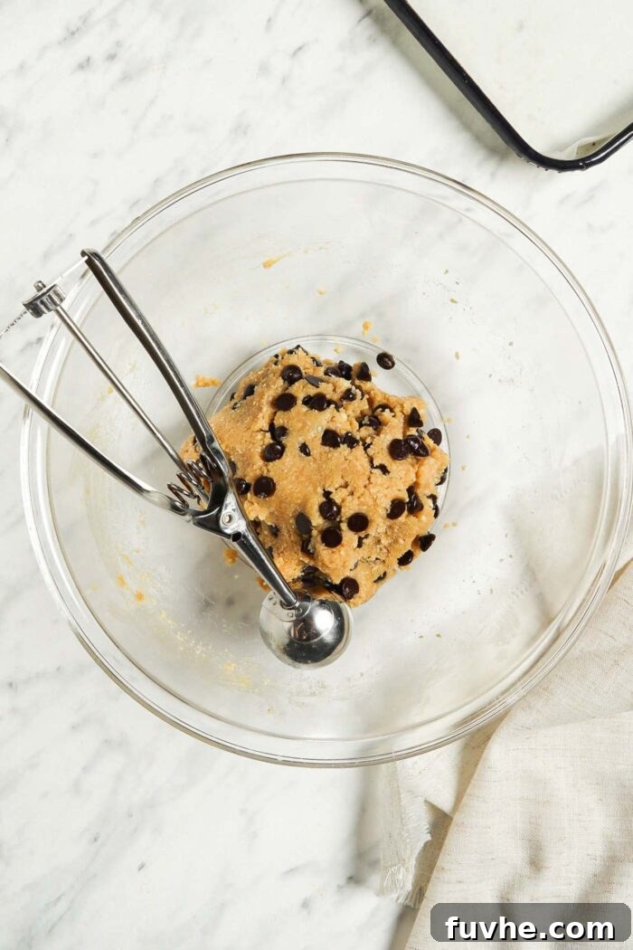Chocolate chip almond flour cookie dough in a glass mixing bowl with a cookie scoop.