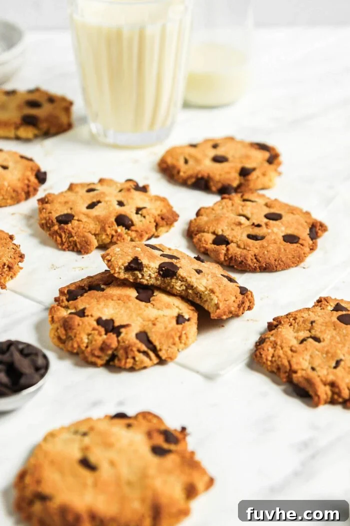 Numerous almond flour chocolate chip cookies on a marble surface with a glass of milk in the background.