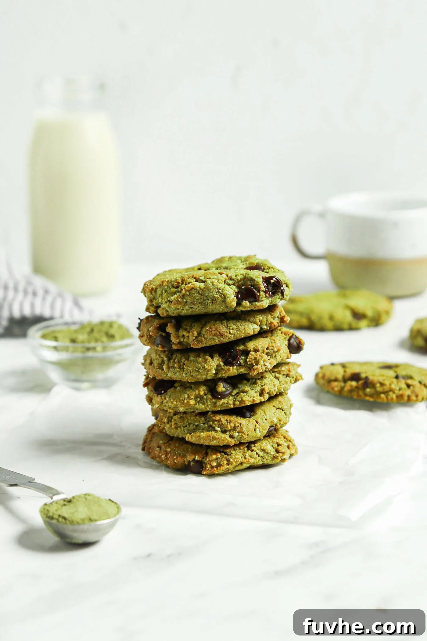 Sublime Vegan Matcha Cookies 2 Stack of almond flour matcha chocolate chip cookies. There's a glass of milk in the background and a tablespoon of matcha powder in the foreground.