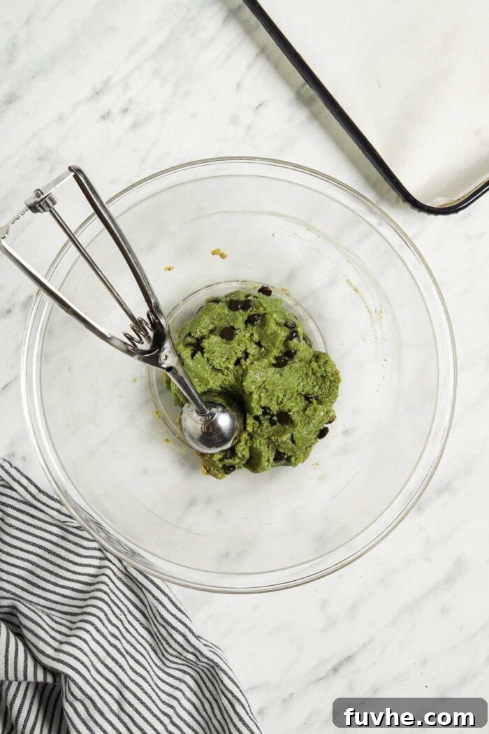 Sublime Vegan Matcha Cookies 4 Raw vegan matcha cookie dough in a glass mixing bowl with a cookie scoop..