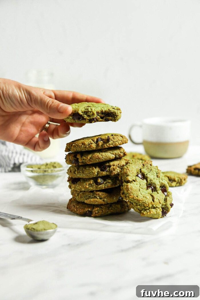Sublime Vegan Matcha Cookies 7 Hand taking a matcha green tea cookie from a stack of cookies on a marble surface.