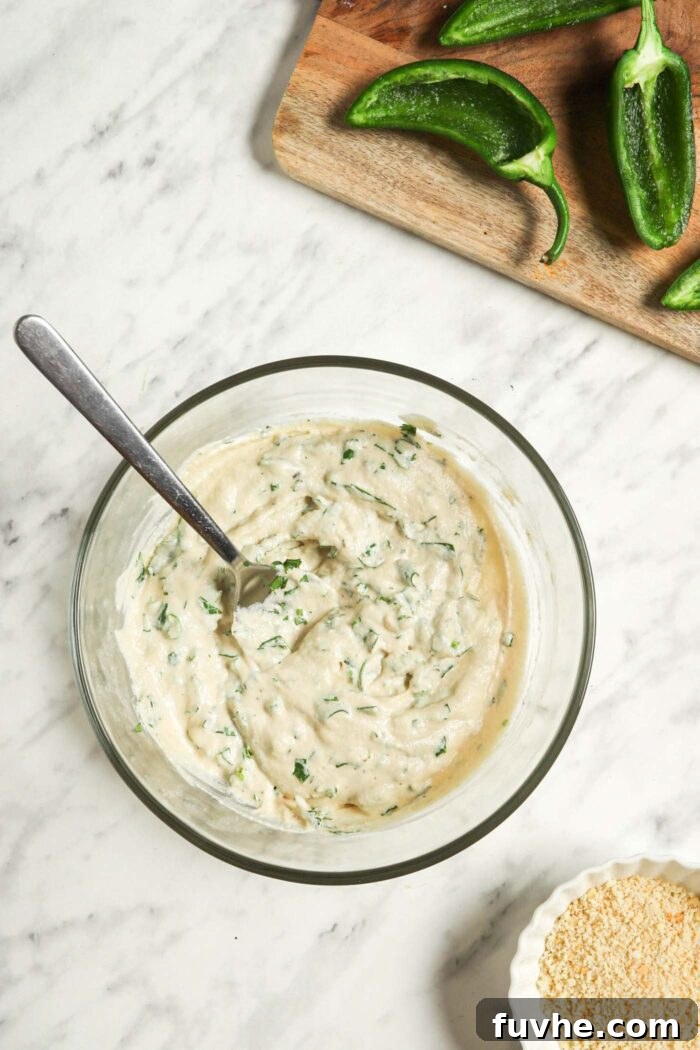 Creamy Vegan Jalapeño Bites 6 Glass mixing bowl containing the creamy cashew filling, now mixed with finely chopped green onions and cilantro, with a spoon ready for filling.