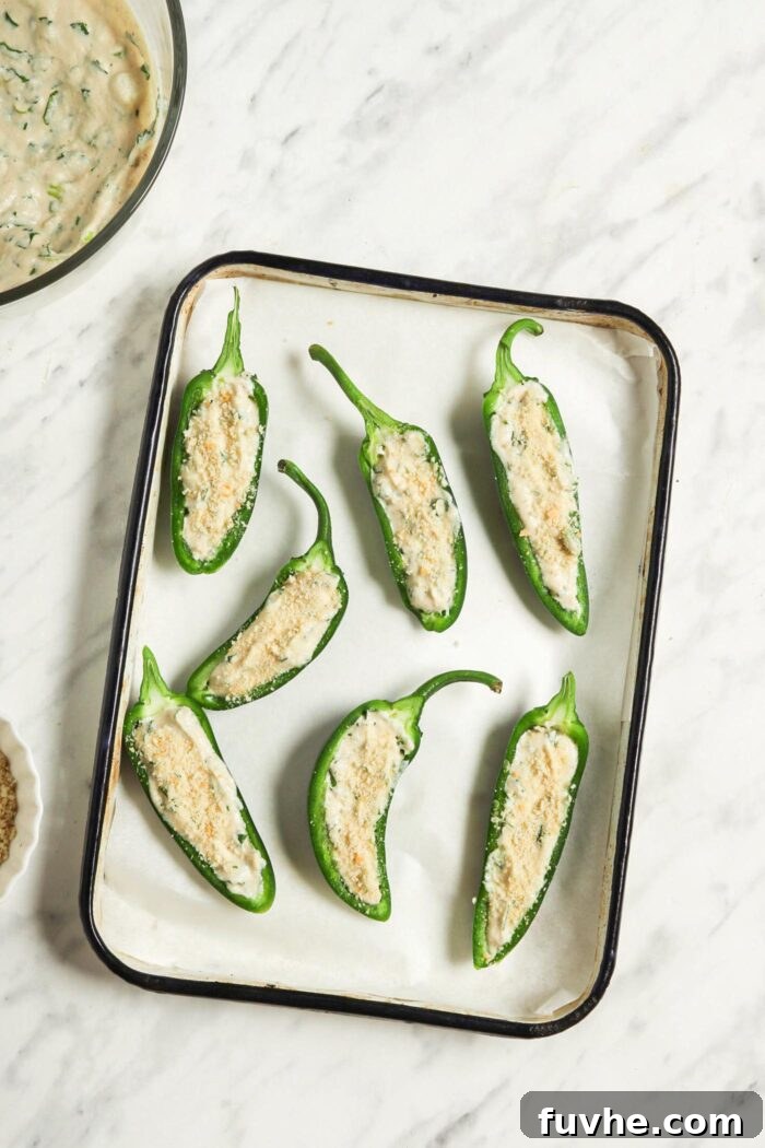 Creamy Vegan Jalapeño Bites 7 Jalapeño halves generously filled with cashew cream and topped with a crispy layer of breadcrumbs, neatly arranged on a parchment-lined baking tray.