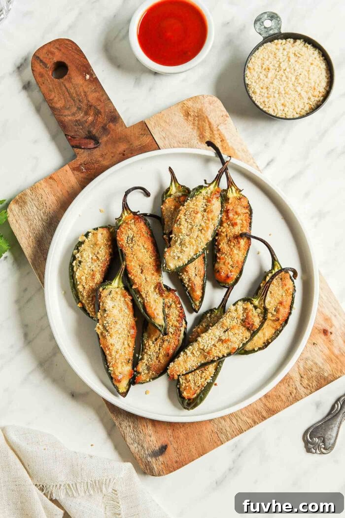 Creamy Vegan Jalapeño Bites 9 A vibrant plate of baked vegan jalapeño poppers, artfully arranged on a rustic cutting board, flanked by small bowls of crispy breadcrumbs and tangy hot sauce, inviting guests to indulge.