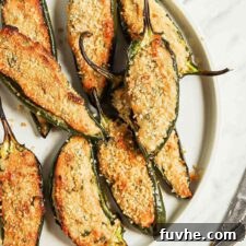 Plate of vegan baked jalapeno poppers sitting on cutting board beside small bowls of breadcrumbs and hot sauce.