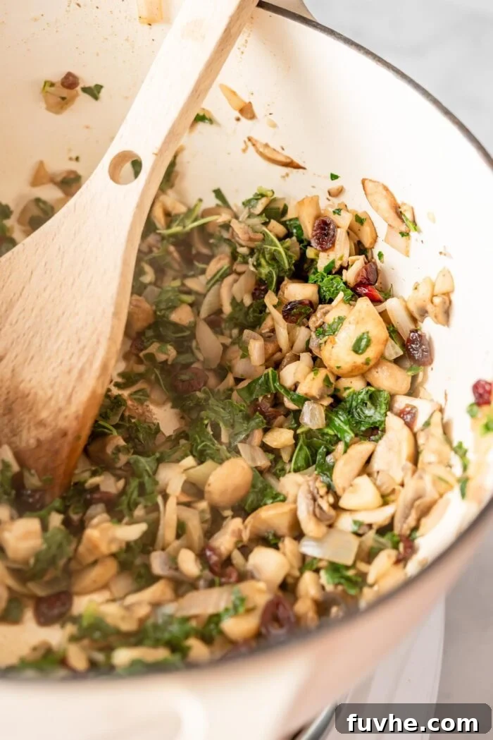 Comforting Vegan Stuffed Butternut Squash 5 Fresh kale, sliced mushrooms, and diced shallots cooking together in a large pot, being stirred with a wooden spoon.