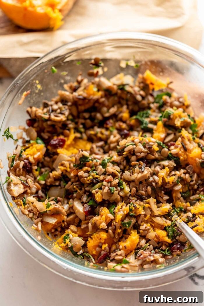 Comforting Vegan Stuffed Butternut Squash 8 A vibrant mix of wild rice, lentils, squash, and kale thoroughly combined in a clear glass mixing bowl, forming the delicious stuffing.