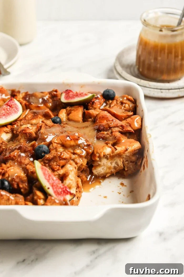 Vegan baked french toast casserole with a slice out of it. Small jar of caramel sauce in the background.