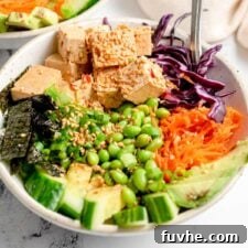 Colorful tofu poke bowl with carrot, cabbage, cucumber, avocado, nori and edamame.