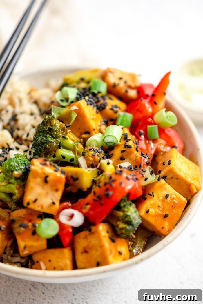 Close up of a bowl of orange tofu and vegetable stir fry topped with black sesame seeds.
