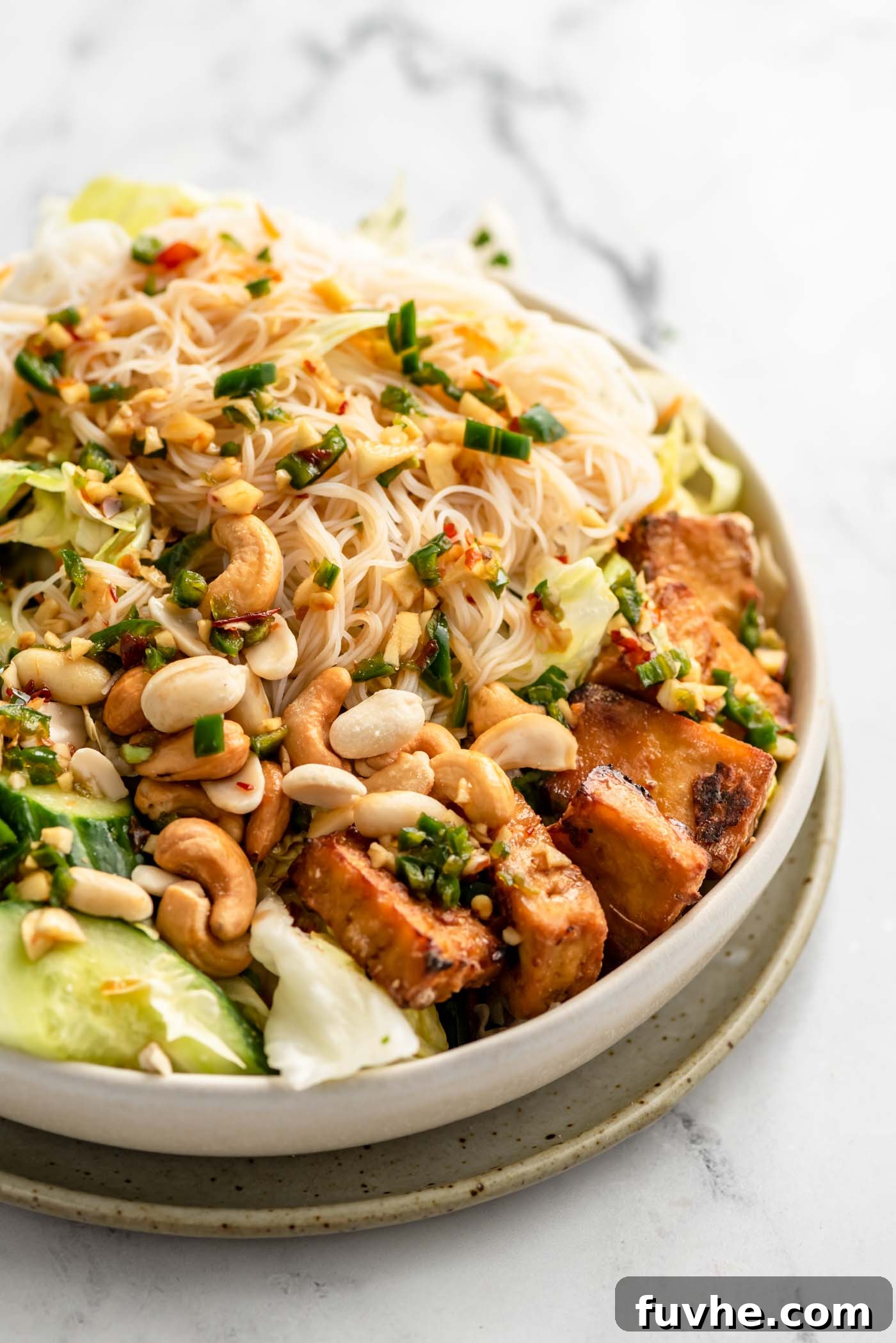 Close up of a vibrant vermicelli noodle salad with crispy tofu, crunchy cashews, fresh lettuce, and sliced cucumber, ready to be enjoyed.