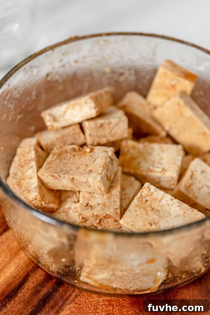 A hand adding thinly sliced tofu pieces and the marinade ingredients into a container, then gently tossing to ensure every piece is coated.