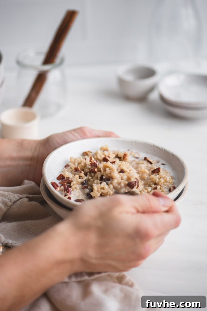 Hand using a spoon in a bowl of brown rice pudding with raisins and coconut milk.