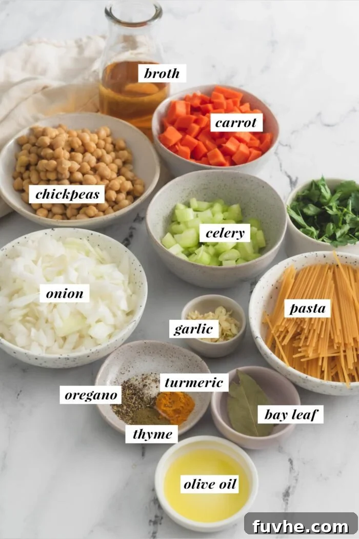 All the essential ingredients meticulously arranged for preparing a delicious vegan chickpea noodle soup, featuring pasta, onion, carrots, celery, and chickpeas.