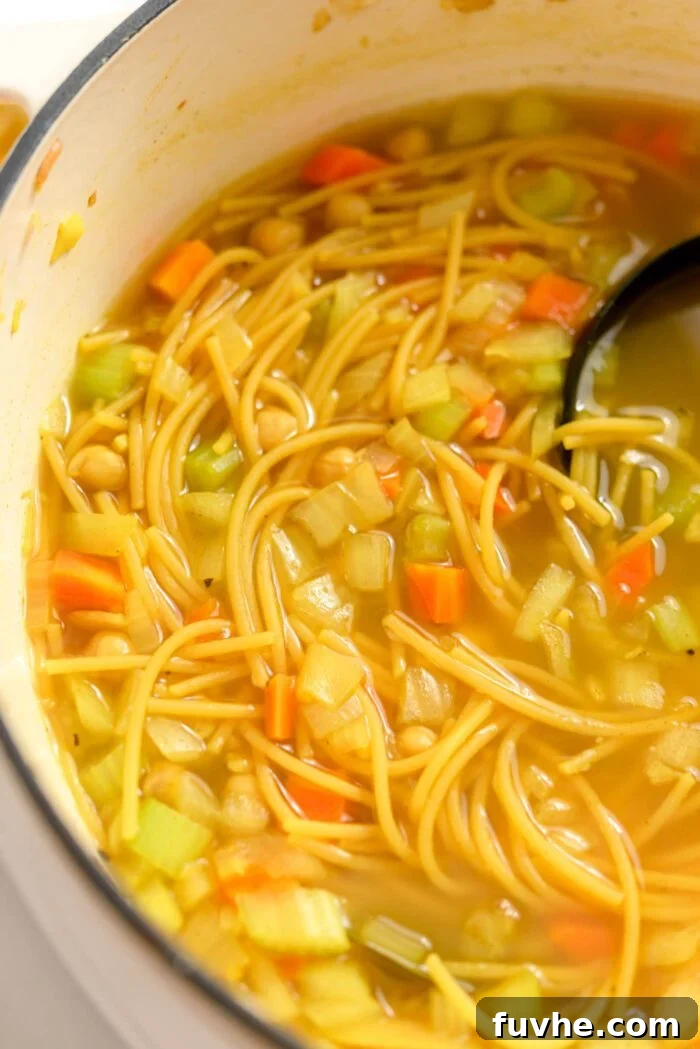 A large pot filled with steaming chickpea noodle soup, featuring a ladle resting within the pot, ready to be served.