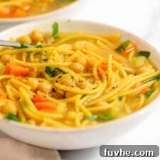 Two bowls of vegan chicken noodle soup with vegetables and spaghetti noodles.