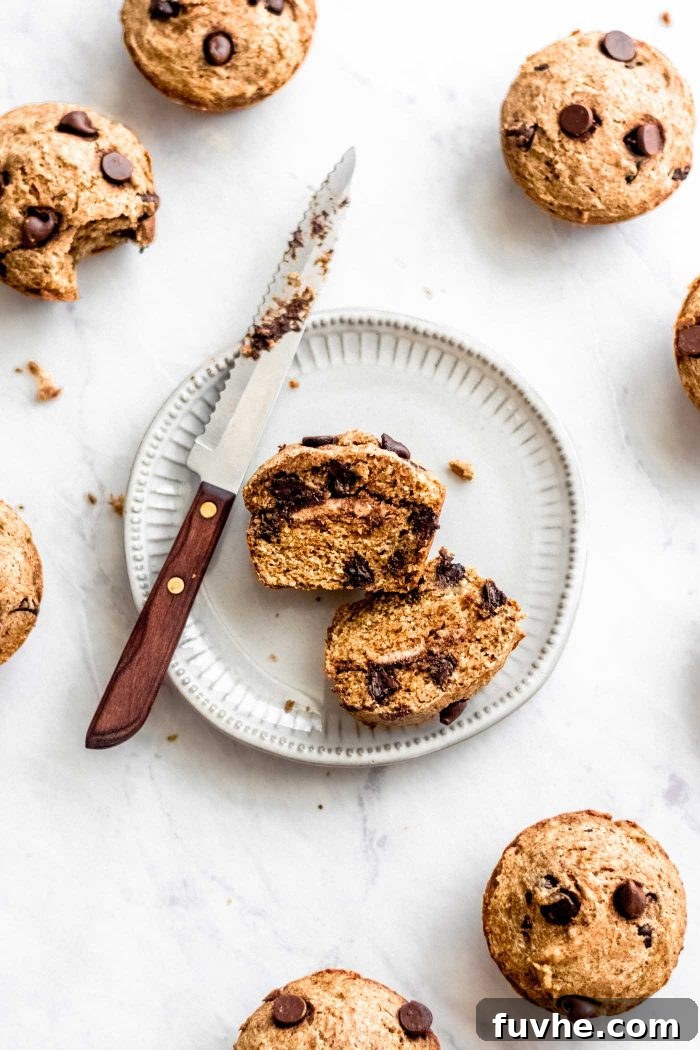Decadent Vegan Chocolate Chip Banana Muffins 6 A freshly baked, sliced vegan chocolate chip banana muffin, revealing its creamy almond butter filling, served on a small white plate with a knife.