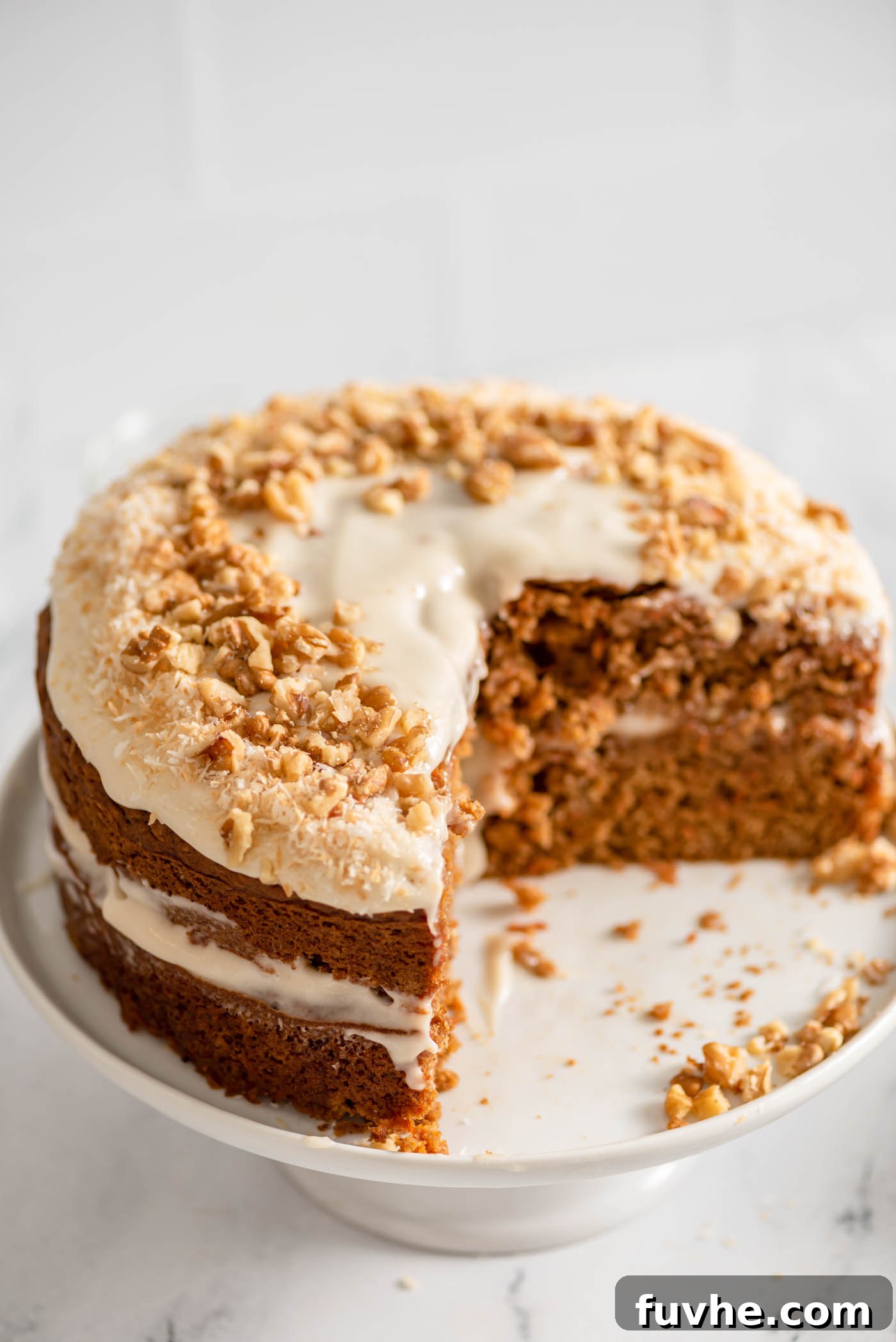 The Perfect Plant-Based Carrot Cake 2 Double layered vegan carrot cake topped with creamy vegan frosting, toasted coconut, and chopped walnuts. A large slice has been cut from it, revealing the moist, spiced interior.