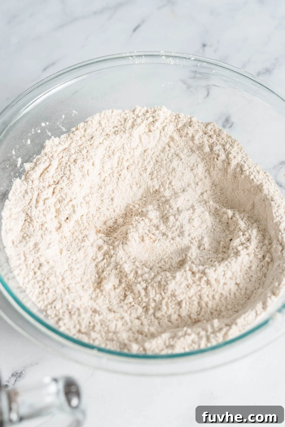 The Perfect Plant-Based Carrot Cake 4 A transparent glass mixing bowl containing flour and a blend of dry spices, perfectly mixed and ready to be combined with wet ingredients.