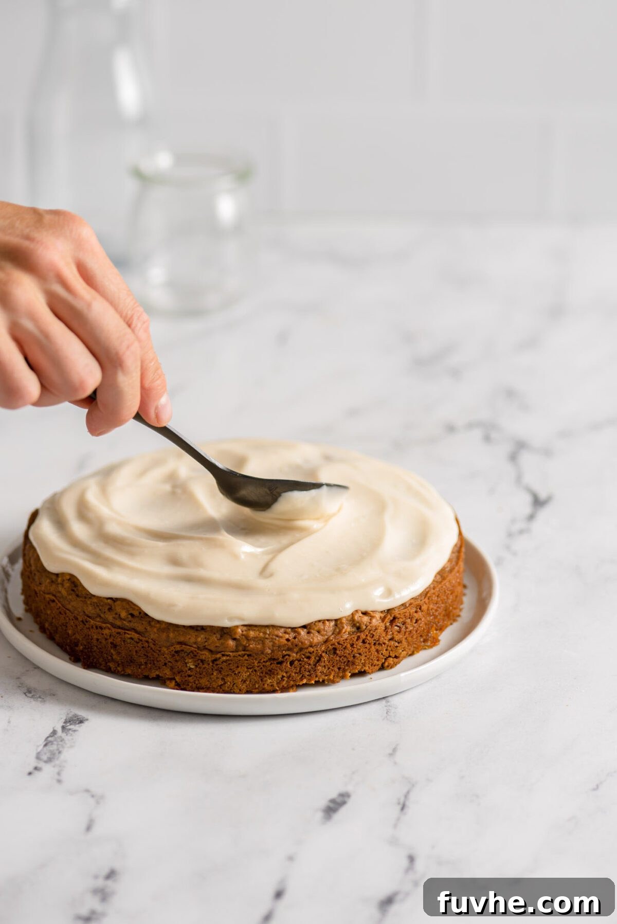The Perfect Plant-Based Carrot Cake 8 Spreading creamy vegan cream cheese frosting smoothly onto the top of a round carrot cake layer with an offset spatula.