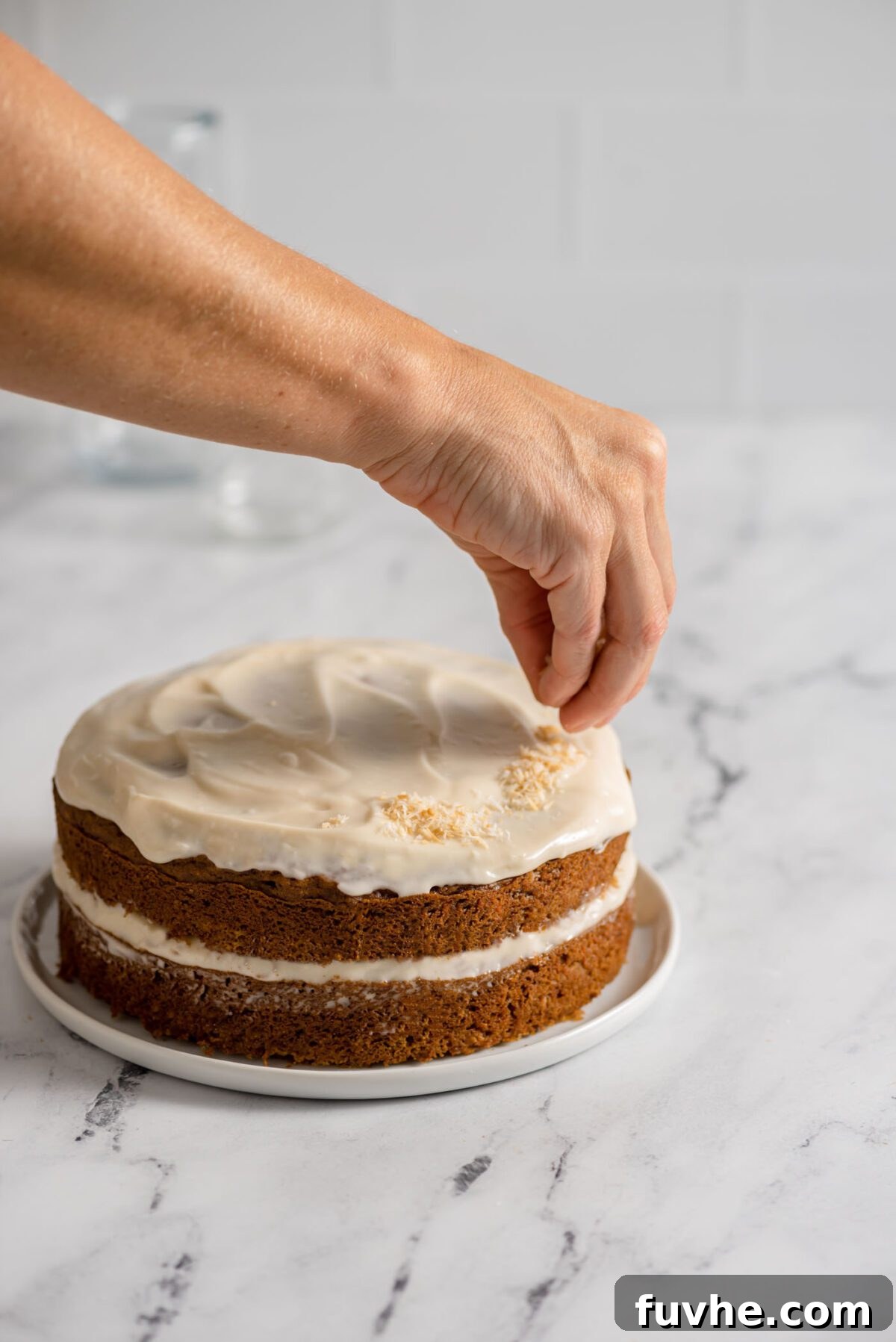 The Perfect Plant-Based Carrot Cake 9 Sprinkling golden toasted coconut flakes over the luscious frosting of a round carrot cake for a beautiful finish.