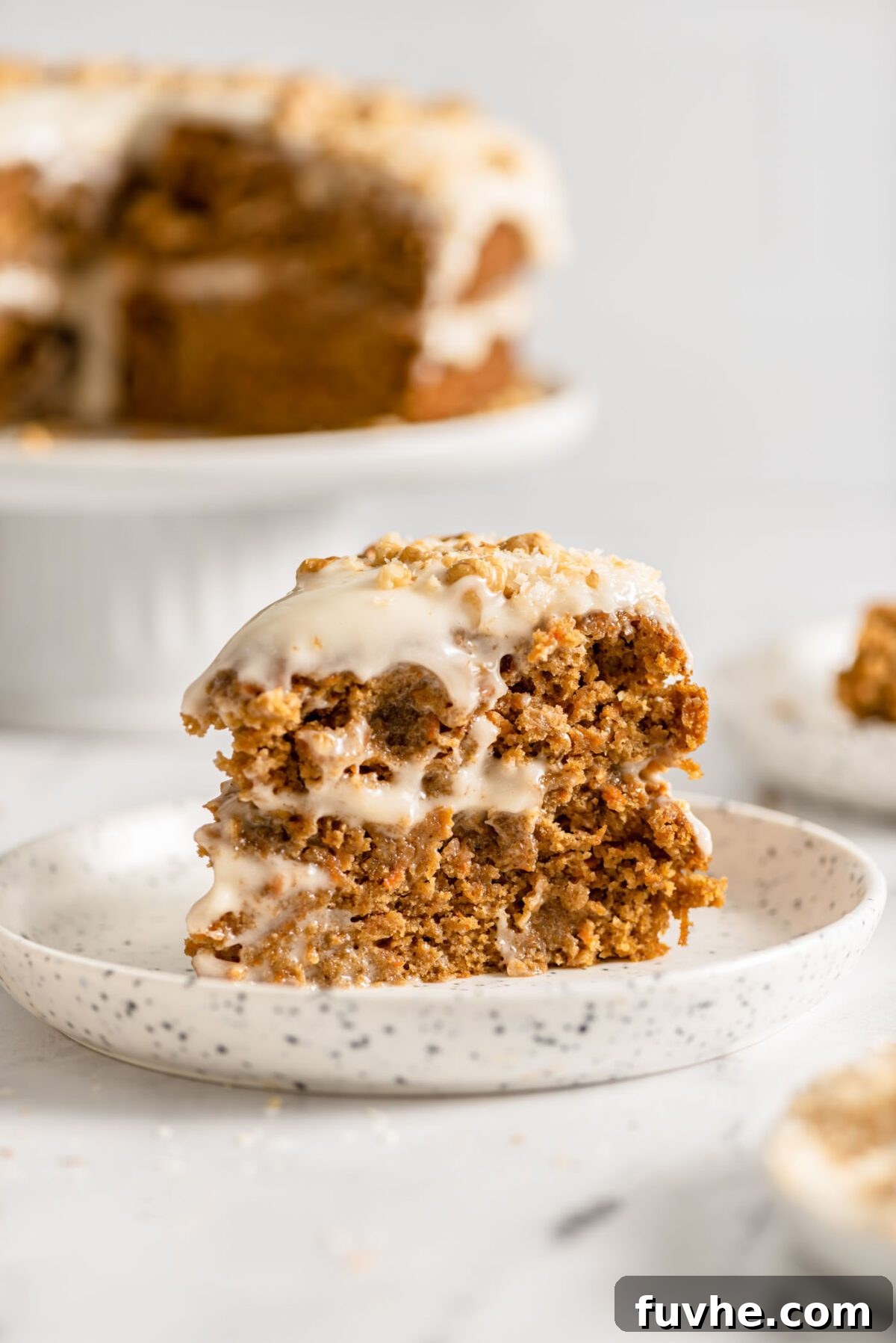 The Perfect Plant-Based Carrot Cake 10 A perfectly portioned slice of double-layered vegan carrot cake, showcasing the rich, creamy frosting and a delicate garnish of chopped walnuts.