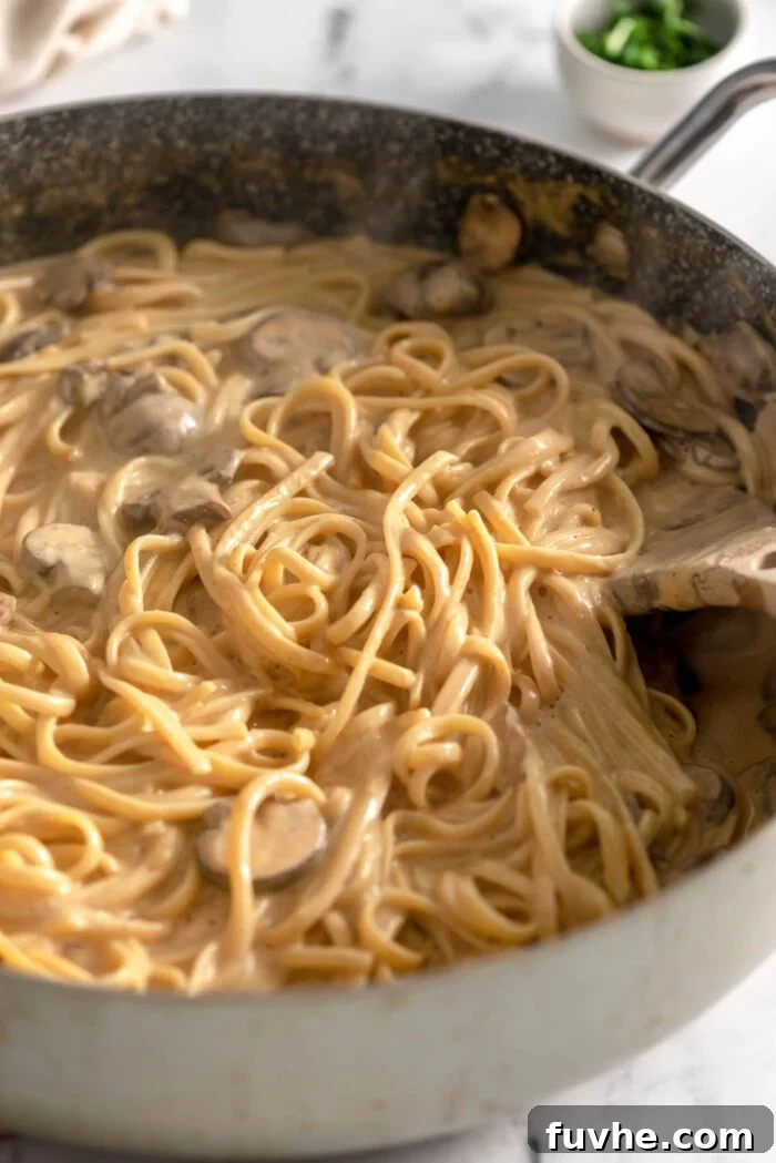 Plant-Based Carbonara 7 Creamy carbonara linguine with mushrooms in a large skillet with a wooden spoon.