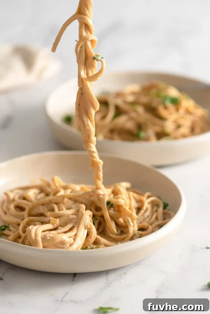 Plant-Based Carbonara 9 Fork lifting a long thread of twirled vegan carbonara pasta from a shallow bowl of pasta.