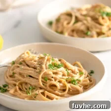 Two bowls of vegan carbonara pasta topped with pepper and chopped parsley in shallow bowls on a marble surface.
