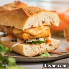Close up of a tofu bahn mi sandwich with spicy mayo and pickled veggies on a plate.