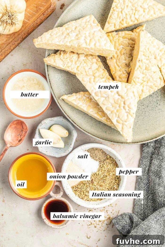 All the fresh ingredients laid out for making a delicious vegan garlic herb seasoned marinated tempeh recipe, including a block of tempeh, fresh garlic, olive oil, and various spices.