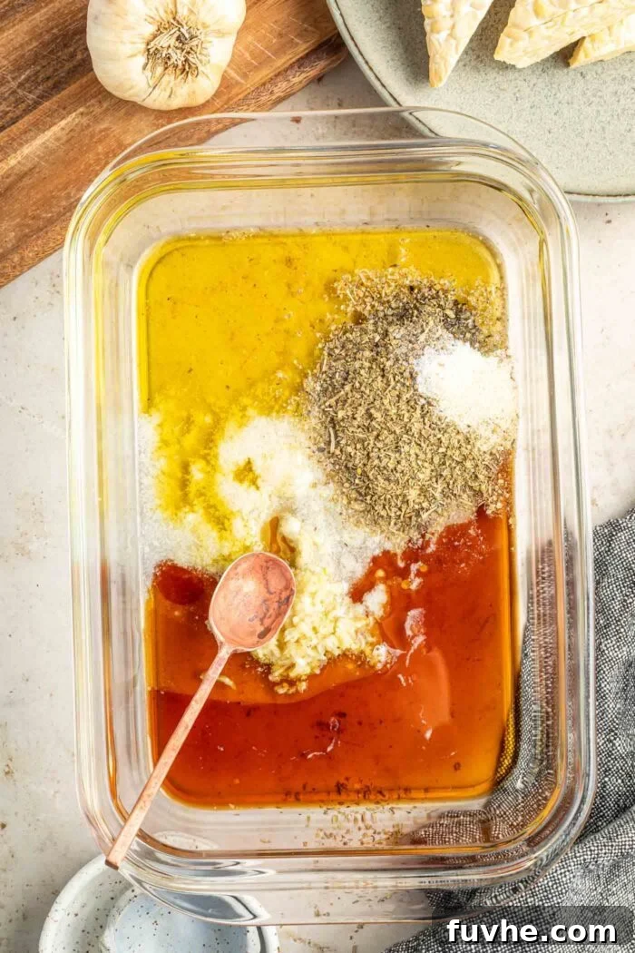 A shallow glass food storage container holding a vibrant tempeh marinade with olive oil, balsamic vinegar, fresh garlic, and various dried herbs, ready to be mixed.