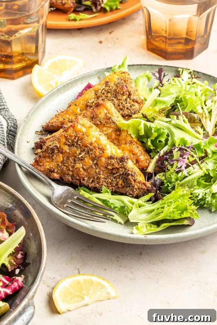 Three perfectly baked garlic herb marinated tempeh pieces on a plate with a vibrant green salad and a fork, emphasizing its role as a satisfying and healthy meal.