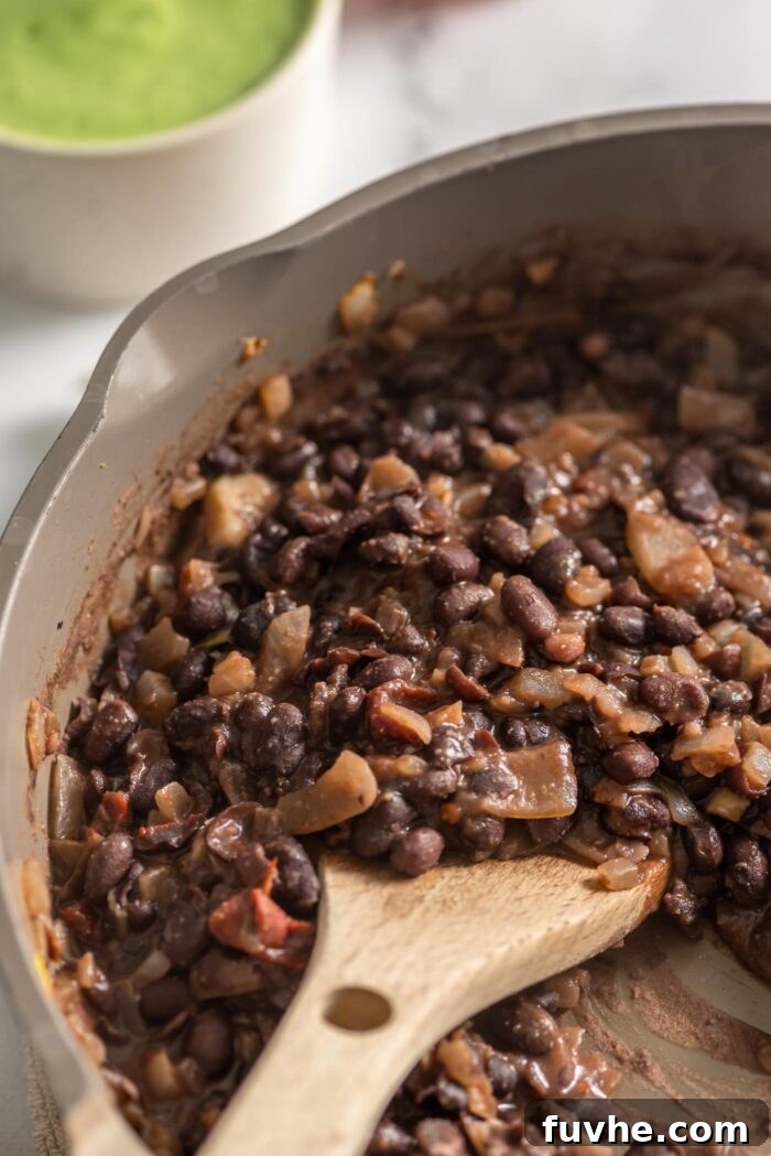 Ultimate Black Bean Tacos 6 Cooked black beans and onions in a skillet with a wooden spoon.