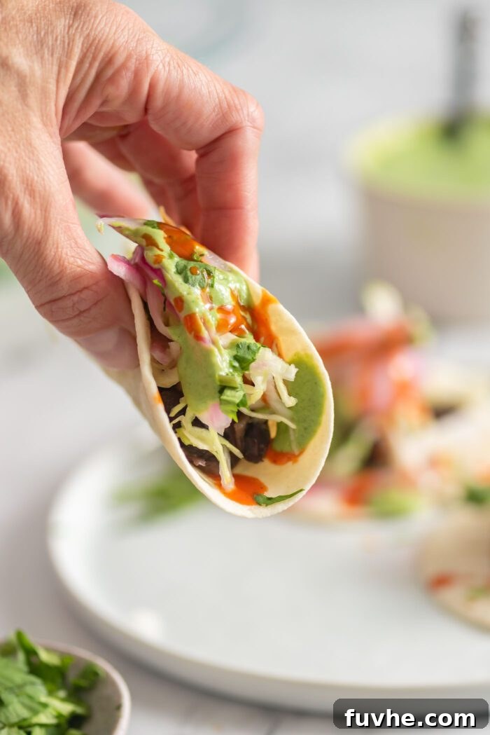 Ultimate Black Bean Tacos 8 Hand holding a black bean taco with hot sauce, cabbage and cilantro lime garlic sauce.