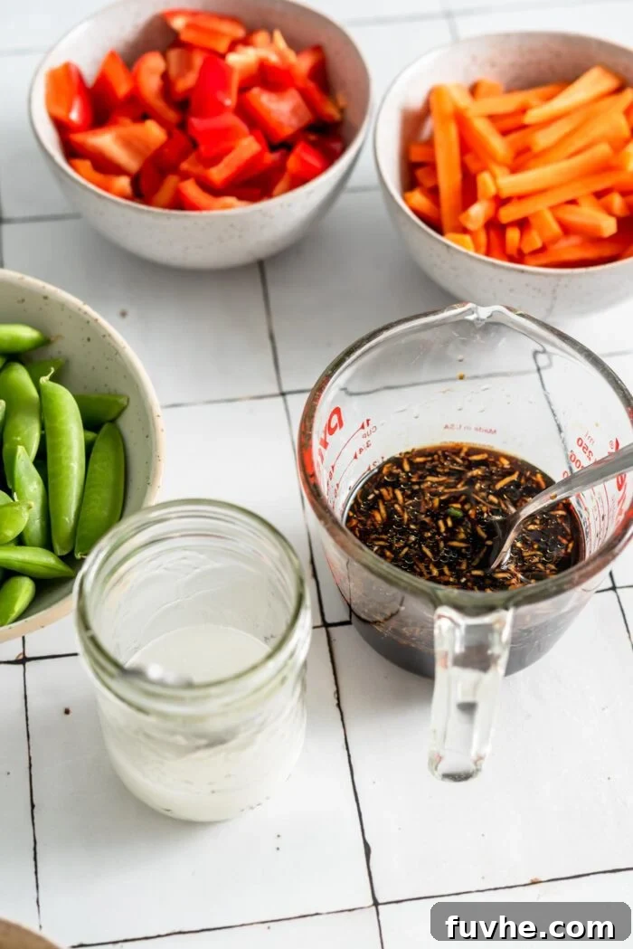 Small glass bowls containing pre-mixed teriyaki sauce and a cornstarch slurry. In the background, various prep bowls hold neatly chopped vegetables, including matchstick carrots, sliced bell peppers, and fresh snap peas, illustrating organized meal preparation.