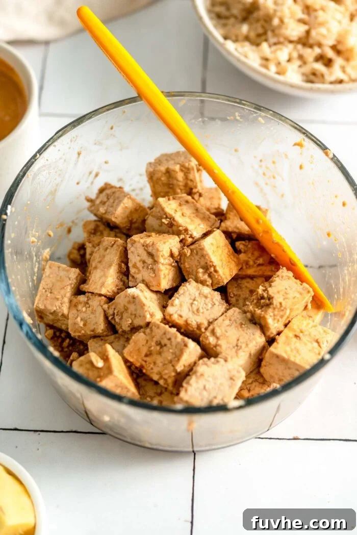 Cubed tofu marinating in sauce in a round glass container.
