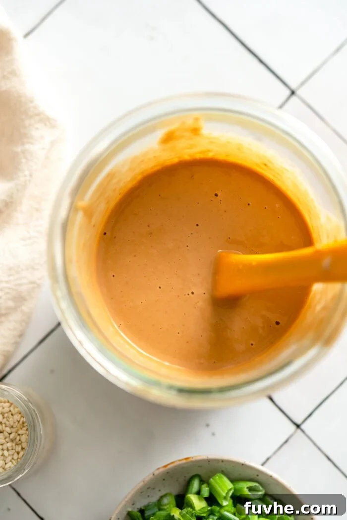 Creamy peanut sauce in a glass jar with a small spatula.