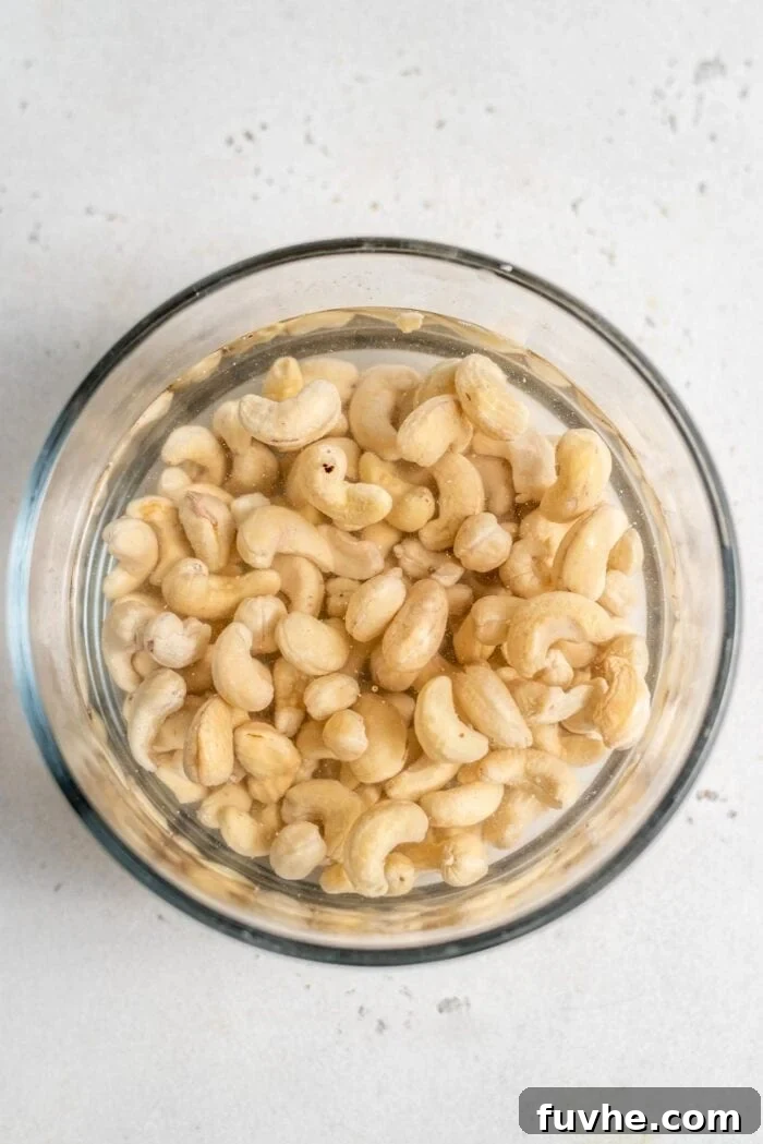Raw cashews soaking in a clear glass bowl, ready for blending into a creamy sauce.