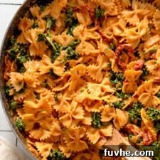 A large pan filled with creamy vegan sun-dried tomato bowtie pasta and kale, served with a wooden spoon.