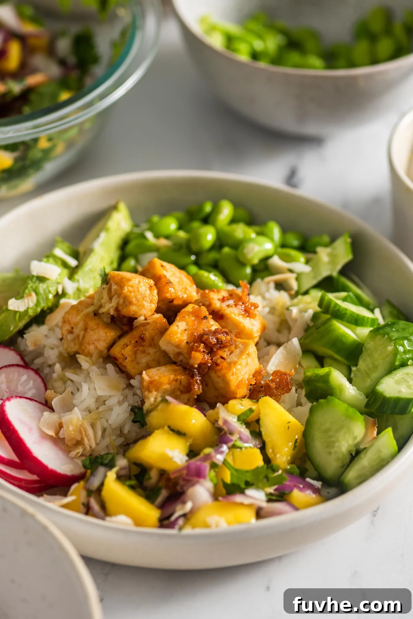 Colourful tofu bowl with mango salsa, edamame, avocado, cucumber, radish and sweet chili tofu, presented beautifully.
