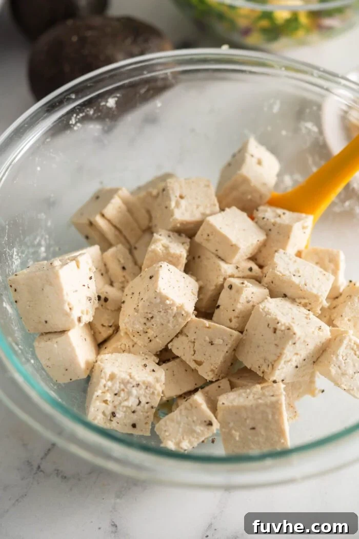 Cubed tofu in a bowl, evenly mixed with cornstarch, salt, and pepper, ready for cooking.