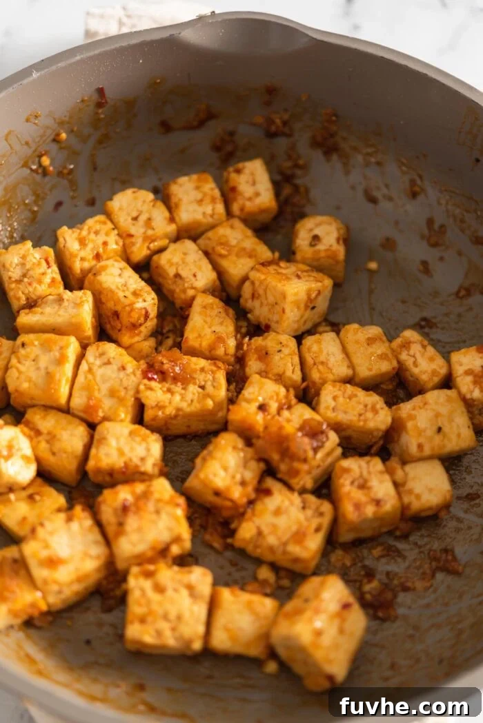 Crispy sweet chili tofu cubes cooking in a skillet, turning golden brown and sizzling.